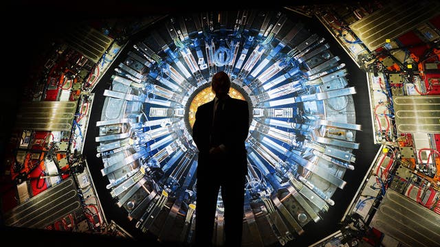 Nobelpreisträger Peter Higgs steht vor dem Foto eines Teilchendetektors