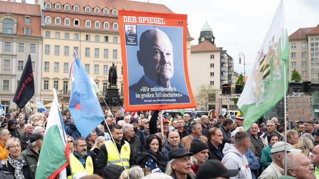 Eine Menschenmenge mit Fahnen und einem Plakat mit einer Titelseite des Nachrichtenmagazins »Der Spiegel«, das Bundeskanzler Olaf Scholz zeigt, stehen auf dem Neumarkt in Dresden.