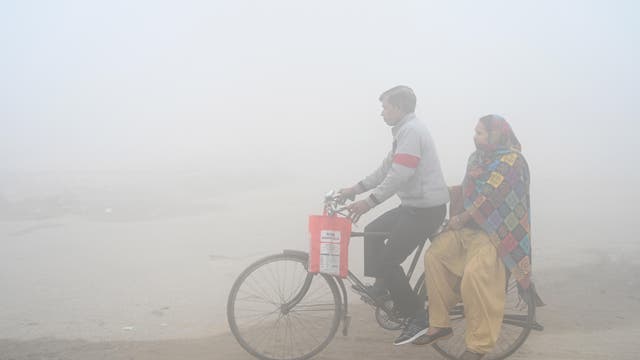 Ein Mann und eine Frau fahren auf einem Fahrrad durch den Smog in Indien