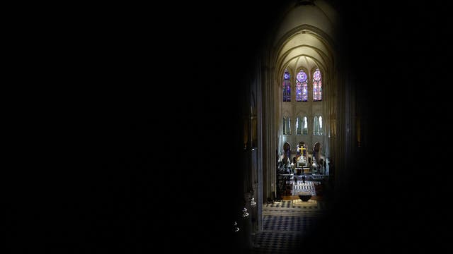 Blick von schräg oben auf den Hochchor von Notre-Dame de Paris mit bunten Glasfenstern und darunter einem Altar, einem Kreuz und einer Statue der Pietà, einer Maria, in deren Schoß der Leichnam von Jesus liegt.