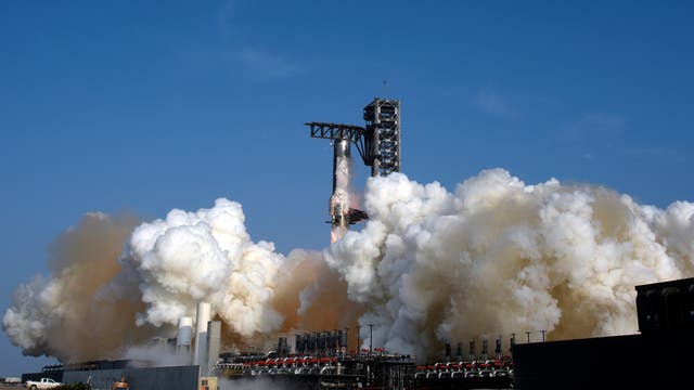Eine Rakete hebt von einer Startrampe ab, umgeben von dichten Rauchwolken und Dampf, die in den blauen Himmel aufsteigen. Die Startrampe ist mit technischen Strukturen ausgestattet, die den Start unterstützen.