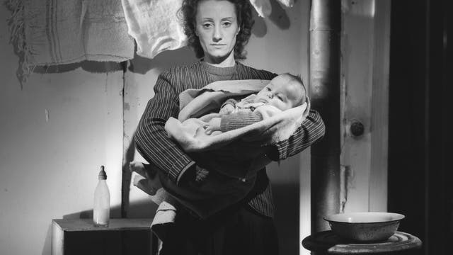 Mutter und Kind vor einem Ofen und einer Wäscheleine. Ein Bild des Fotografen Lucien Lorelle aus dem Jahr 1946.