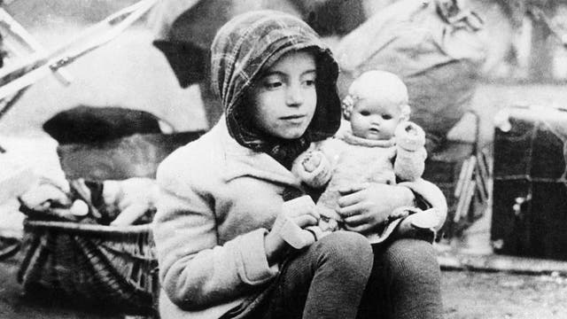 Ein Mädchen, das zu einem Flüchtlingstreck in der Nachkriegszeit gehört, hält seine Puppe im Arm.