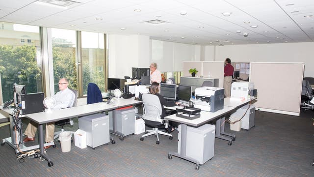 Ein Büroraum mit mehreren Tischen, auf denen sich diverse Büromaterialien und ein Computermonitor befinden.