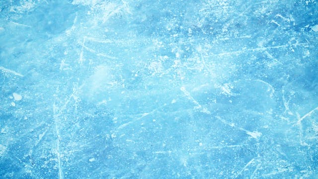 Eine Nahaufnahme einer eisigen Oberfläche mit einer hellblauen Tönung. Die Textur zeigt Kratzer und unregelmäßige Muster, die an gefrorenes Wasser erinnern. Die Oberfläche wirkt rau und uneben, was auf eine natürliche Eisbildung hinweist.