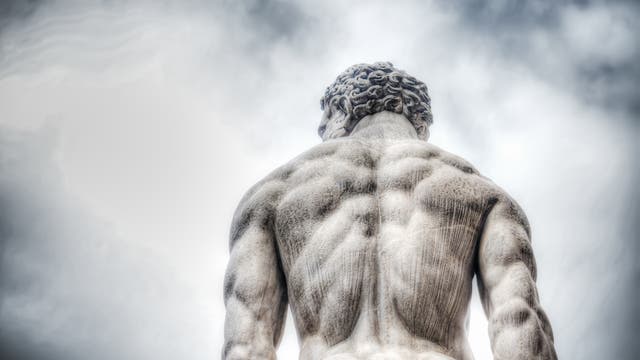 Sehr muskulöse Rückenpartie einer Herkulesstatue aus Stein vor dramatischem Himmel.