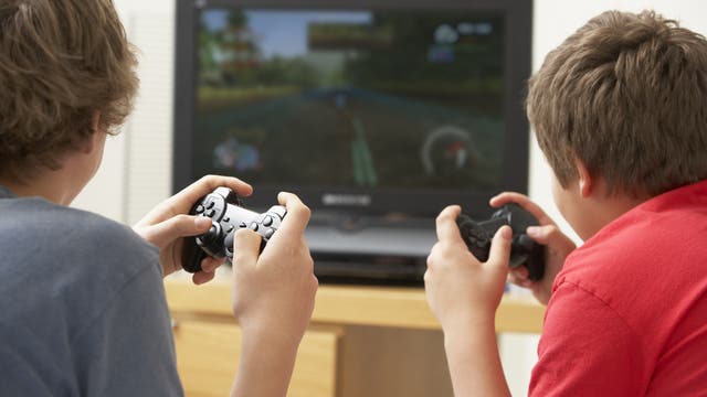 Zwei Jungs von hinten, sie spielen ein Computerspiel mit Spielekonsole und schauen auf einen Bildschirm, jeder hält einen Controller in der Hand.