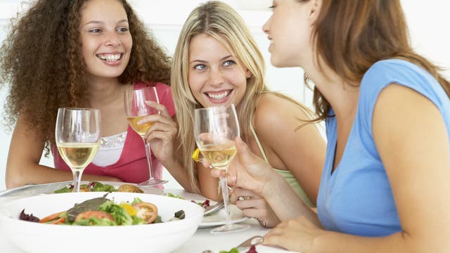 Drei Freundinnen sitzen daheim beim Essen zusammen, sie unterhalten sich fröhlich miteinander.