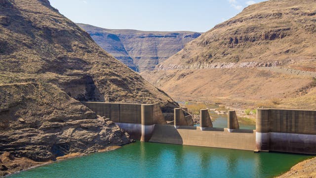 Ansicht des Wasserkraftwerks in Lesotho zwischen kargen Bergen, das Wasser ist grün-blau.
