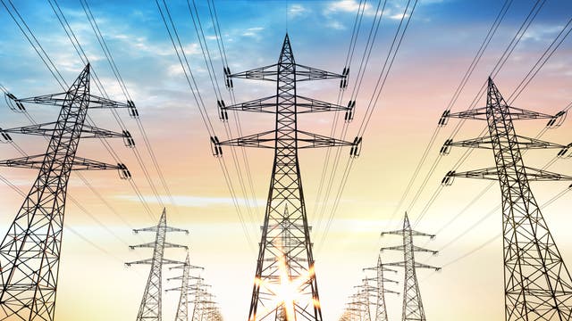 Mehrere Strommasten stehen in einer Reihe und tragen elektrische Leitungen, die sich in die Ferne erstrecken. Der Himmel im Hintergrund zeigt einen Farbverlauf von Blau zu Orange, was auf einen Sonnenauf- oder -untergang hindeutet. Die Szene vermittelt ein Gefühl von Weite und Energieinfrastruktur.