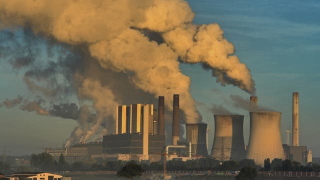 Ein Kohlekraftwerk mit rauchenden Schornsteinen vor blauem Himmel.