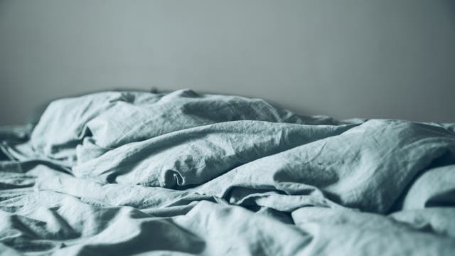 Zerwühltes, leeres Bett mit grau-blauer Decke/Laken