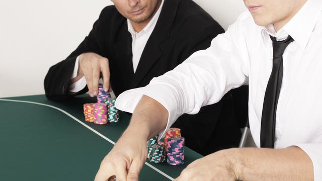 Zwei Kartenspieler an einem Tisch, einer mischt die Karten, der andere schaut ihn misstrauisch an. 
