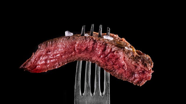 Ein Stück medium rare Steak auf einer Gabel vor schwarzem Hintergrund