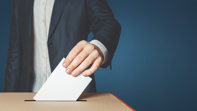 Stimmzettelabgabe: Eine Hand steckt einen Stimmzettel in eine Wahlbox
