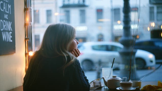 Frau alleine im Cafe, stützt das Kinn auf die Hand und schaut aus dem Fenster.