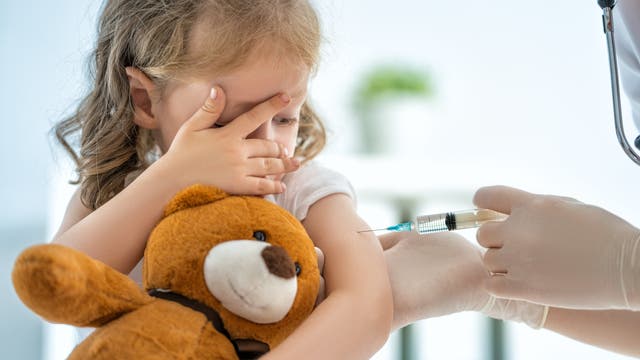 Ein Kind hält bei der Impfung einen Teddy.