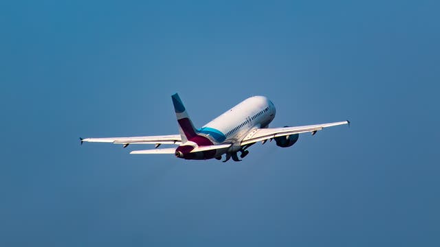 Ein Passagierflugzeug hebt in den blauen, wolkenlosen Himmel ab. Die Triebwerke sind sichtbar und das Fahrwerk wird gerade eingezogen. 