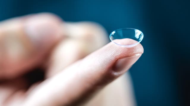 Makroaufnahme einer Hand, die eine Kontaktlinse auf einer Fingerspitze hält. 