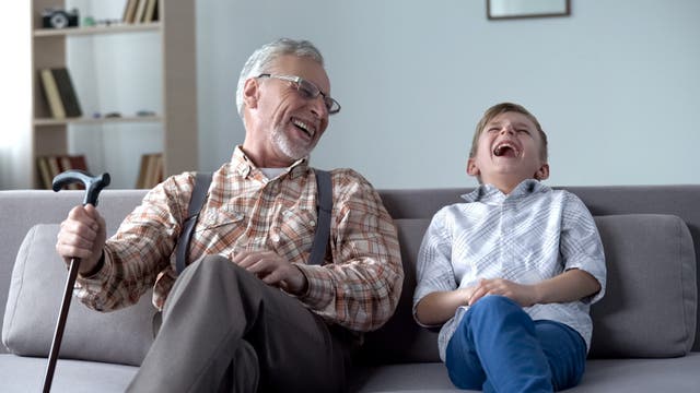 Ein alter Mann und ein Junge sitzen auf dem Sofa und lachen lauthals