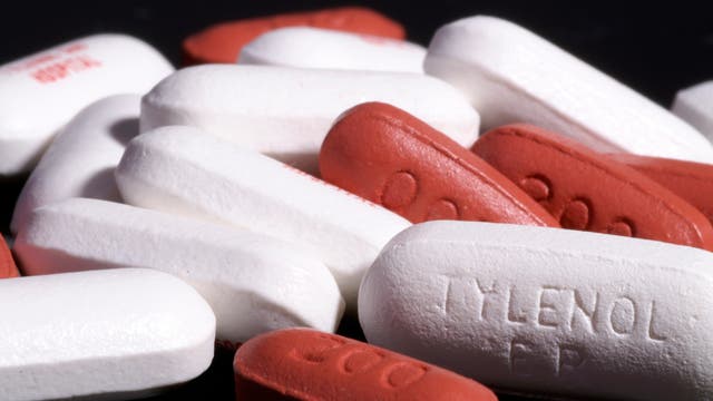 Eine Nahaufnahme von mehreren weißen und roten Tabletten auf schwarzem Hintergrund. Auf einer der weißen Tabletten ist der Text "TYLENOL ER" eingeprägt. Die roten Tabletten haben die Zahl "500" eingeprägt. Das Bild zeigt eine Mischung von Medikamenten in Kapselform.