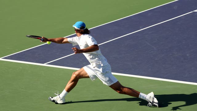 Ein Tennisspieler in weißer Kleidung hechtet auf dem Platz einem Ball hinterher. 