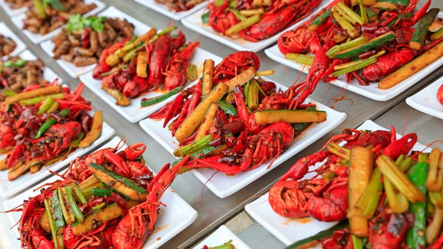 Eine Reihe von Tellern, die mit gekochten Flusskrebsen und Gemüse wie Frühlingszwiebeln und Gurken garniert sind. 