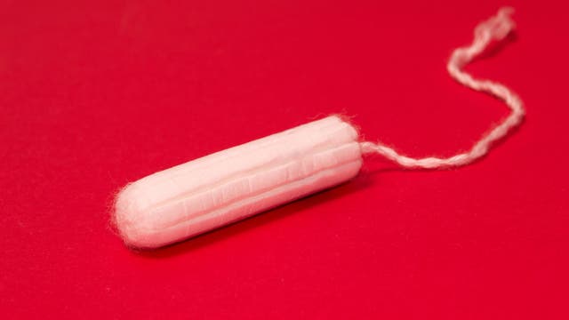 Ein weißer Tampon mit Rückholfaden liegt auf einem roten Hintergrund. Das Bild hebt die kontrastreiche Farbe hervor und betont die Hygiene und den Gebrauch von Tampons.