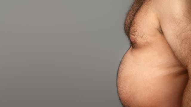 Ein Foto zeigt den seitlichen Oberkörper eines Menschen mit freiem Oberkörper vor einem grauen Hintergrund. Der Fokus liegt auf dem Bauchbereich.
