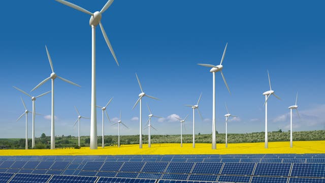 Windkrafträder und Solarmodule vor gleißend blauem Himmel, im Hintergrund gelbe Rapsfelder