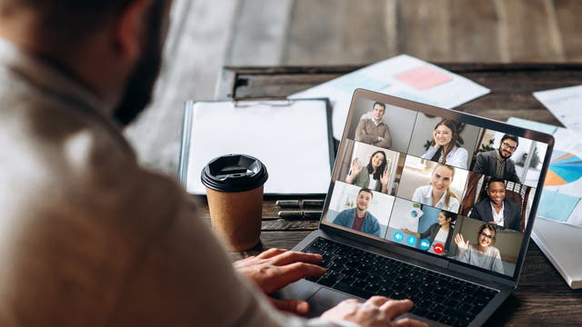 Ein Mann sitzt vor einem Laptop und befindet sich in einem virtuellen Meeting mit Kollegen.