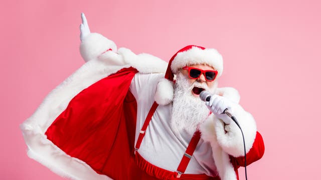 Ein Weihnachtsmann mit roter Sonnenbrille singt mit Mikrofon vor einem pinken Hintergrund 