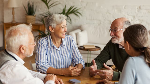 Senioren sitzen lachend am Tisch und spielen Karten