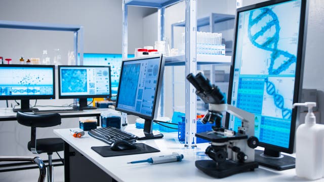 Innenraum eines Labors mit Geräten wie Mikroskopen und großen Bildschirmen mit darauf gezeigten Gendaten.