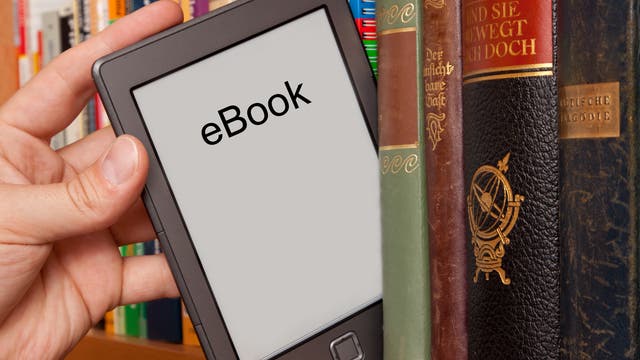 Eine Hand nimmt ein E-Book zwischen Büchern aus dem Bücherregal.