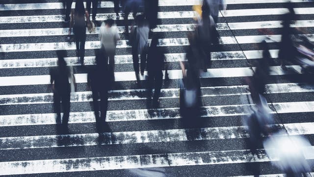 Menschen überqueren schnellen Schrittes einen Fußgängerüberweg auf dem Weg zur Arbeit