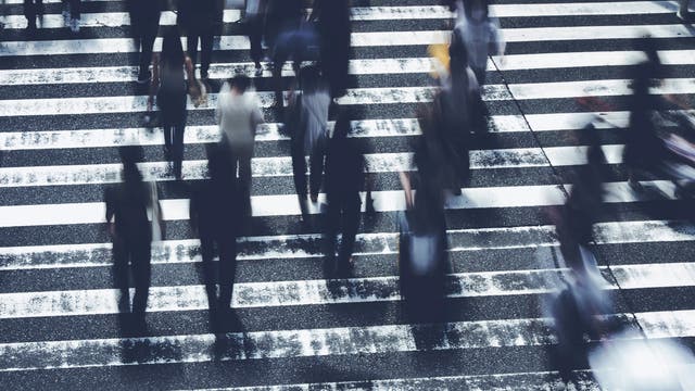 Menschen überqueren schnellen Schrittes einen Fußgängerüberweg auf dem Weg zur Arbeit