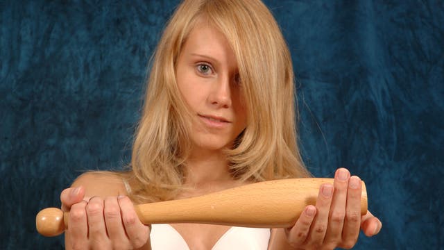 Eine blonde Frau hält eine kurze Gymnastikkeule in die Kamera.