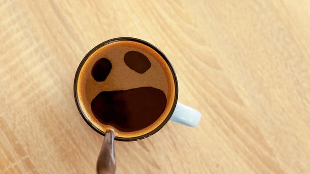 Blick von oben auf eine Kaffeetasse; der Schaum hat drei Öffnungen wie zwei Augen und offener Mund.