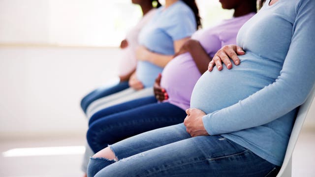 Vier schwangere Frauen sitzen in einer Reihe auf Stühlen in einem Wartezimmer