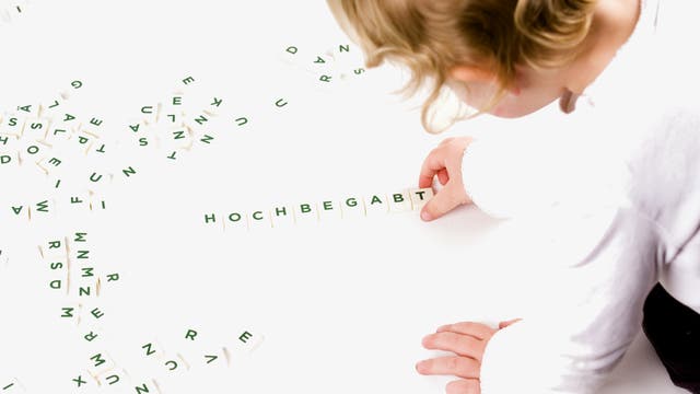 Ein Kind legt das Wort "hochbegabt" mit Scrabble-Steinchen. Tatsächlich hat es natürlich ein Erwachsener gelegt und dann auf den Auslöser gedrückt. Das Bild stellt also nicht die Eigenschaften des Kindes dar, sondern Wünsche und Erwartungen von Erwachsenen, passend zum Thema.
