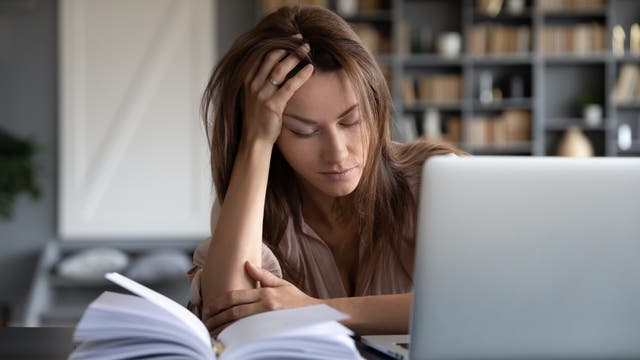 Eine junge Frau sitzt mit geschlossenen Augen und aufgestütztem Kopf vor dem Laptop.