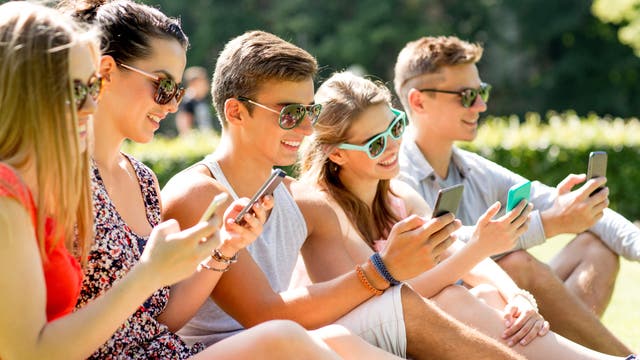 Junge Menschen sitzen mit Smartphone in der Sonne