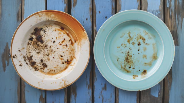 Zwei verkrustete, dreckige Essteller auf einem Holztisch