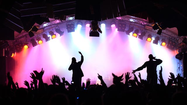 Eine Konzertbühne mit Band und Lightshow, davor Publikum.