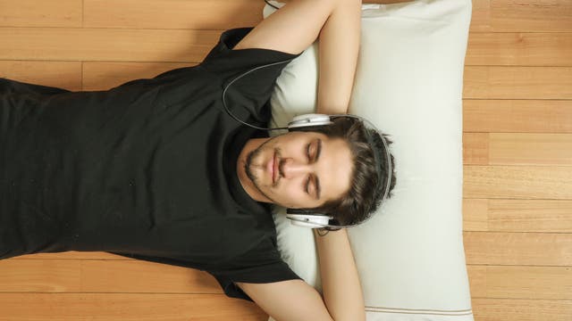 Mann mit Kopfhörer liegt entspannt mit geschlossenen Augen