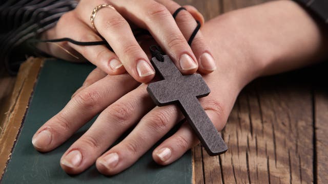 Zwei Hände halten einen hölzernen Kreuzanhänger.