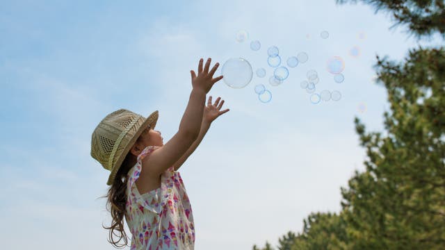Szene in der Natur: ein Kind versucht Seifenblasen in der Luft zu fangen.