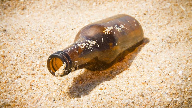 Eine leere braune Flasche ohne Etikett liegt im Sand.