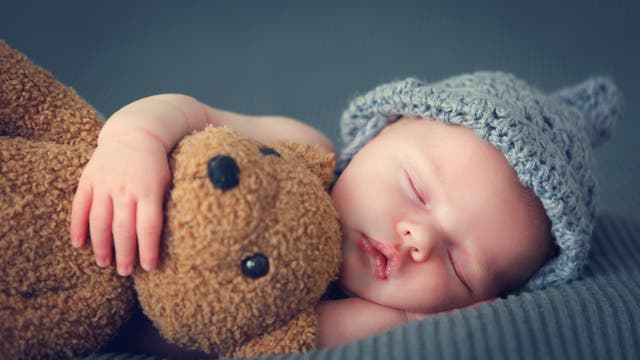 Schlafendes Baby mit Mütze und Stofftier 